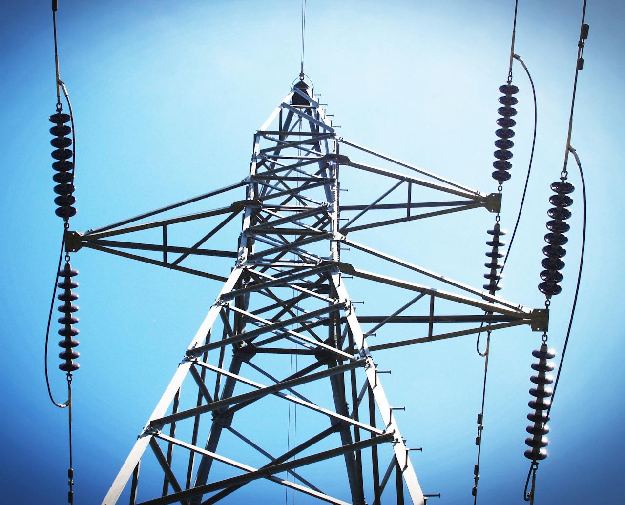 stats-img Low angle view of an industrial power transmission tower against a clear blue sky.