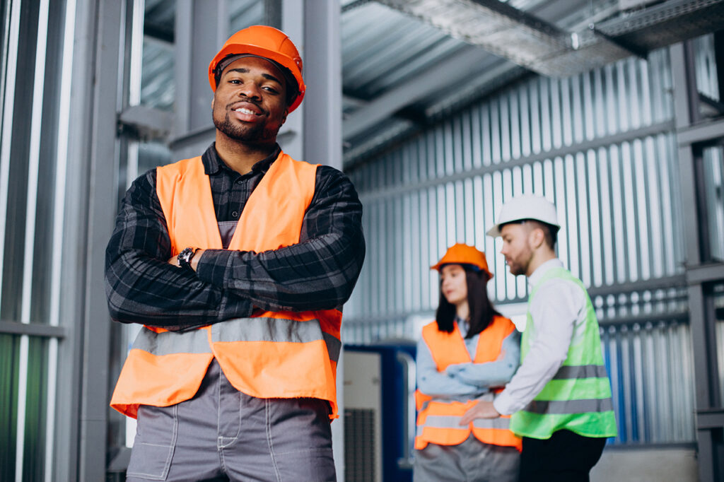 three factory workers in safety hats discussing manufacture plan